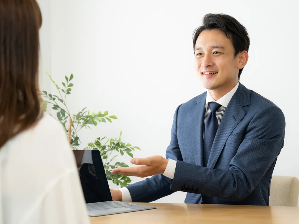明るいオフィスで、笑顔で相談に乗るスーツ姿の男性税理士と女性の相談者
